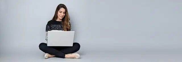 Woman sitting cross-legged using a laptop on a gray background.