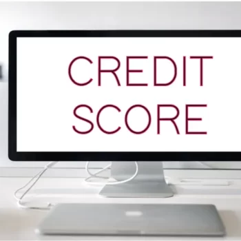Computer monitor on a desk displaying the words "CREDIT SCORE" in bold red font.