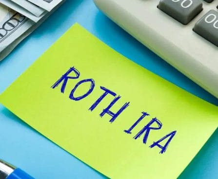 A sticky note with "ROTH IRA" written on it, next to cash, a calculator, and a pen on a blue background.