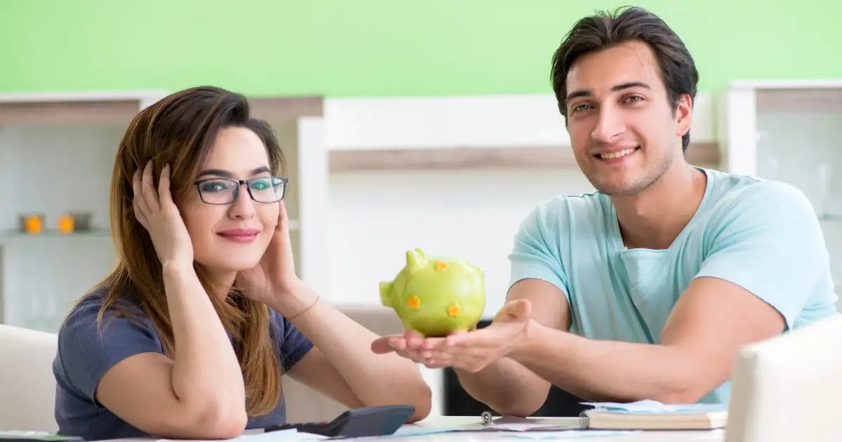 Two smiling people with a piggy bank at a table, possibly discussing finances.